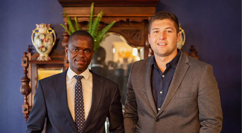 Two men in suits standing in front of a framed portrait